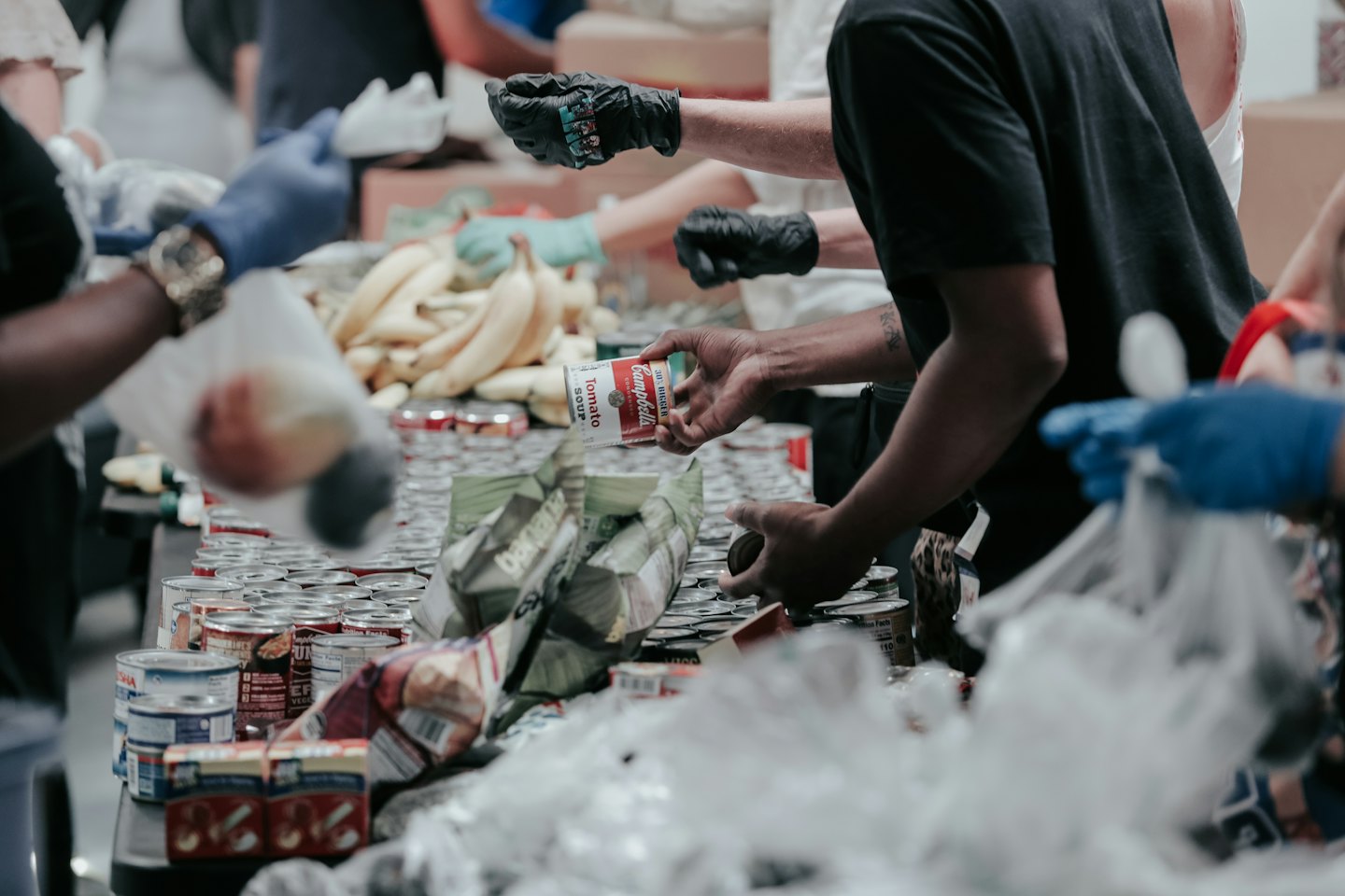 Volontari smistano cibo in scatola e banane durante un evento di distribuzione alimentare.
