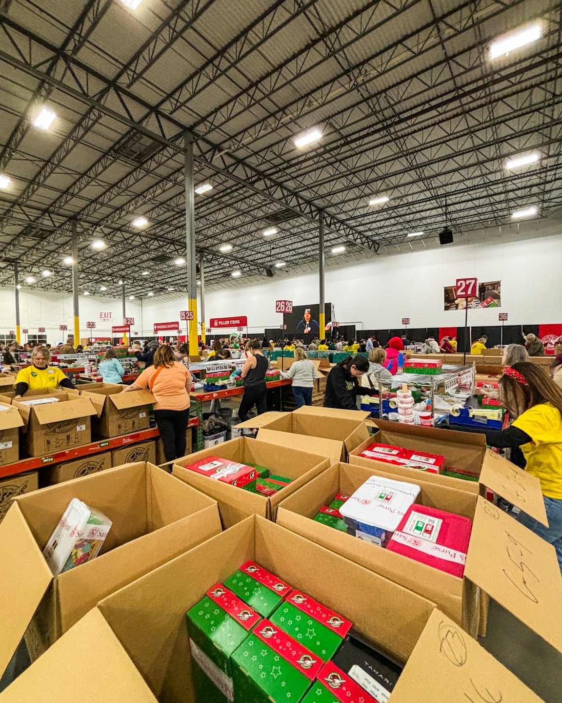 Volontari diversi impacchettano regali di Natale in scatole in un magazzino.
