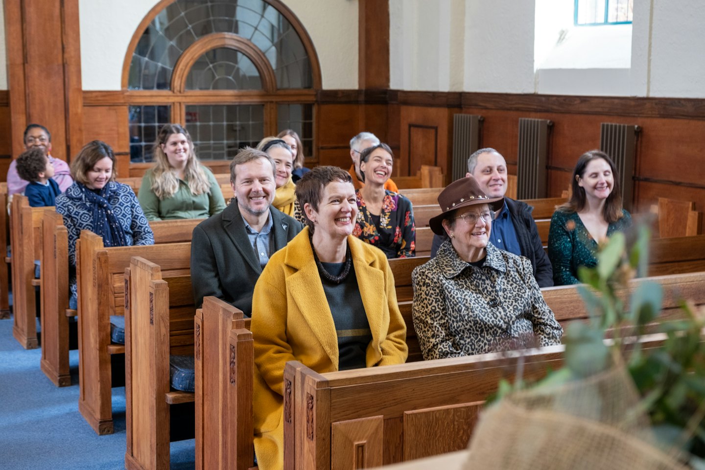 Persone sorridenti sui banchi della chiesa guardano verso un evento.